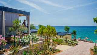 Udsigt over en moderne lodge med blomsterhave og panoramaudsigt til havet under en klar blå himmel.