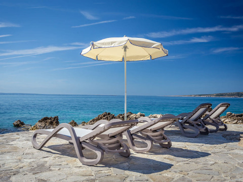Vier Liegestühle und ein Sonnenschirm am Meer im Valamar Camping Ježevac, Primorje-Gorski Kotar, Kroatien.