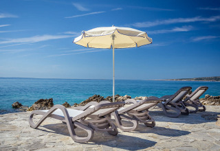Vier Liegestühle und ein Sonnenschirm am Meer im Valamar Camping Ježevac, Primorje-Gorski Kotar, Kroatien.