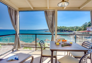 Terraza cubierta con vistas al mar, mesa de comedor y tumbonas en Valamar Camping Ježevac, Croacia.
