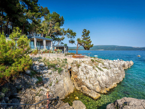 Vista de la costa rocosa en Valamar Camping Ježevac, Croacia, con mar claro, árboles y bungalows.