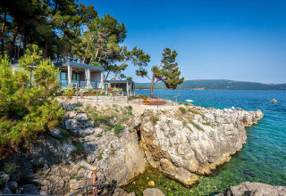 Vista sulla costa rocciosa del Valamar Camping Ježevac in Croazia con mare limpido e case mobili.
