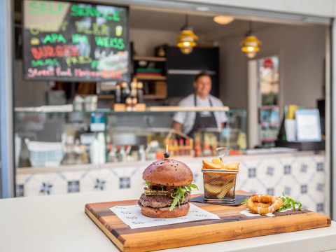 Ein saftiger Burger und Pommes werden auf einem Holzbrett vor einem Imbiss im Valamar Camping Ježevac serviert.