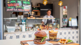 Una jugosa hamburguesa con papas fritas servidas en una tabla frente a un puesto en Valamar Camping Ježevac, Croacia.