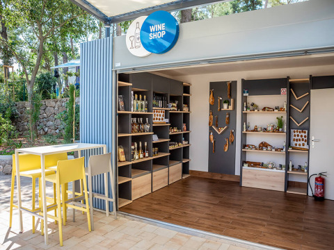 Tienda de vinos moderna al aire libre en Valamar Camping Ježevac, Croacia, con estantes y mesa de degustación.