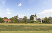 Landelijk vakantiepark met glamping, traditionele windmolen, huizen met rode daken en groene velden.