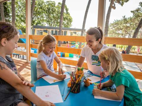 Kinder und eine Betreuerin zeichnen gemeinsam an einem Tisch im Freien im Ferienpark Valamar Camping Ježevac.