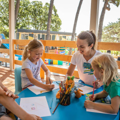 Niños y una monitora realizan actividades creativas en una mesa exterior en Valamar Camping Ježevac, Croacia.