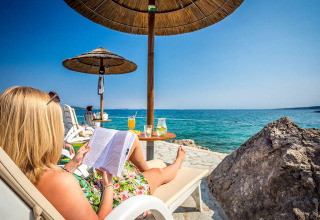 Donna che si rilassa su una sdraio vicino al mare, leggendo un libro sotto un ombrellone al Valamar Camping Ježevac.