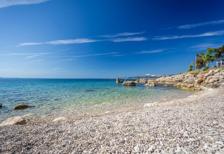 Spiaggia di ciottoli con mare cristallino e cielo azzurro a Valamar Camping Ježevac, Croazia, estate.