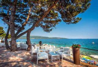 Terrasse mit weißen Sitzmöbeln am Meer unter Pinien bei Valamar Camping Ježevac, Kroatien, im Sommer.