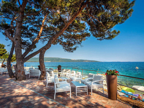 Terrasse mit weißen Sitzmöbeln am Meer unter Pinien bei Valamar Camping Ježevac, Kroatien, im Sommer.