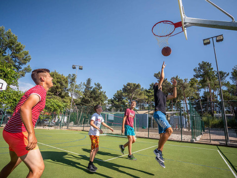 Vier Personen spielen Basketball im Freien bei Valamar Camping Ježevac in Kroatien unter blauem Himmel.