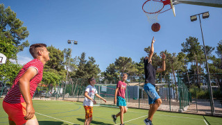 Cuatro personas juegan baloncesto al aire libre en Valamar Camping Ježevac, Croacia, bajo el cielo azul.