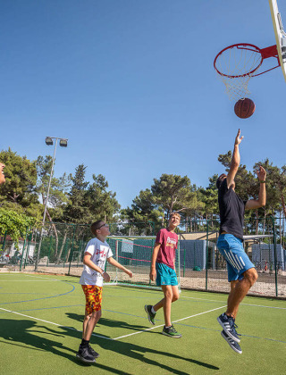Four people enjoy an outdoor basketball game at Valamar Camping Ježevac, Croatia, on a sunny day.