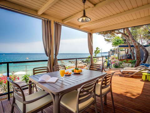 Terraza cubierta con mesa, sillas y vista al mar en Valamar Camping Ježevac, Primorje-Gorski Kotar, Croacia.