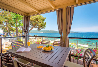 Covered terrace with table, chairs, and sea view at Valamar Camping Ježevac in Primorje-Gorski Kotar, Croatia.