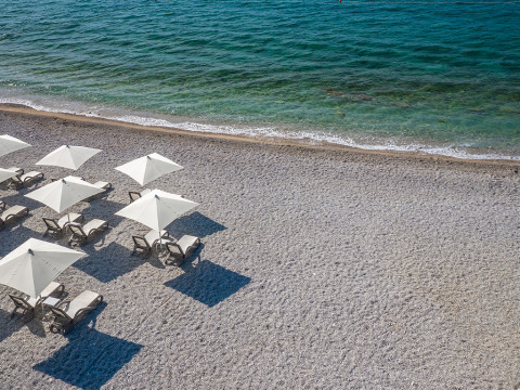 Leere Liegestühle und weiße Sonnenschirme am Kieselstrand von Valamar Camping Ježevac, Kroatien, am Meer.