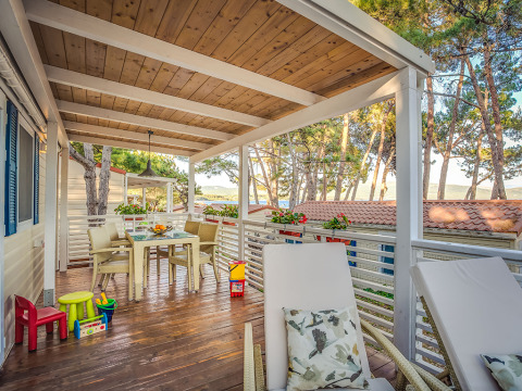 Covered outdoor terrace at Ježevac Home lodge with sea view, dining table, loungers, and kids' toys.