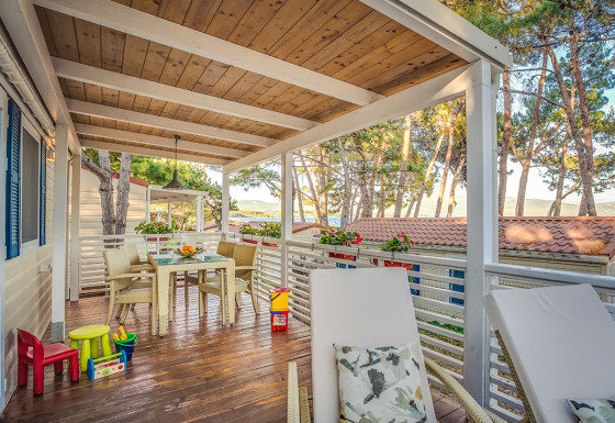 Covered outdoor terrace at Ježevac Home lodge with sea view, dining table, loungers, and kids' toys.