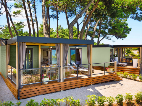 Moderne Lungomare Home lodge met houten terras, omgeven door dennenbomen in een rustige natuuromgeving.
