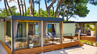 Moderne Lungomare Home lodge met houten terras, omgeven door dennenbomen in een rustige natuuromgeving.