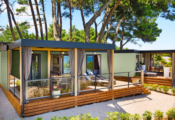 Moderne Lungomare Home lodge met houten terras, omgeven door dennenbomen in een rustige natuuromgeving.