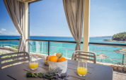 Terrazza di lodge sul mare con sedie grigie, succo d'arancia, arance e lavanda vista mare blu limpido.