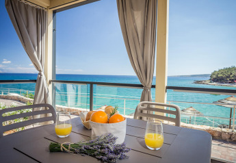 Terrazza di lodge sul mare con sedie grigie, succo d'arancia, arance e lavanda vista mare blu limpido.