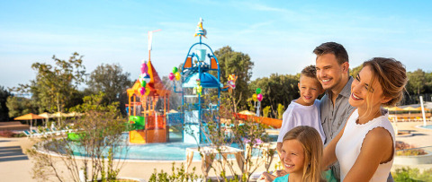 Famille souriante devant une aire de jeux aquatique colorée à Valamar Camping Istra, Istrie, Croatie.
