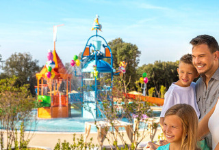 Famille souriante devant une aire de jeux aquatique colorée à Valamar Camping Istra, Istrie, Croatie.