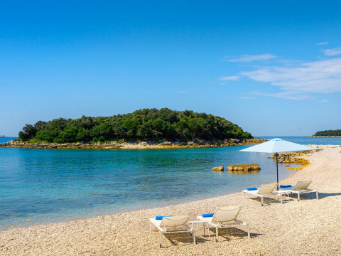 Strandblick auf Valamar Camping Istra in Istrien, Kroatien, mit Liegestühlen und Sonnenschirm am klaren Wasser.