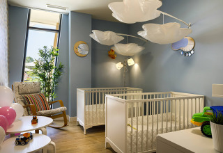 Modern nursery room with two white cribs, cloud-shaped lamps, and toys at Valamar Camping Istra in Croatia.