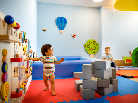 Bambini piccoli giocano in una colorata stanza giochi con blocchi e attività a parete in un parco vacanze in Istria.