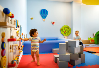 Peuters spelen in een kleurrijke indoor speelkamer met blokken en wandspellen in een vakantiepark in Istrië.