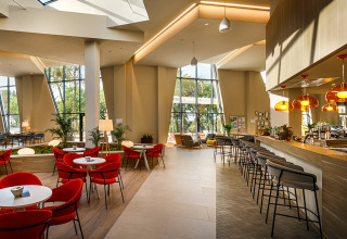 Cafetería luminosa y moderna con sillas rojas, barra y grandes ventanales en Valamar Camping Istra en Croacia.