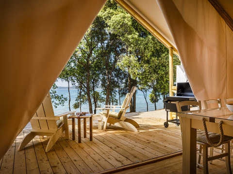 View from tent veranda with wooden chairs at Valamar Camping Istra, overlooking sea and trees in Croatia.