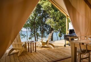Zicht vanop een tentveranda met houten stoelen bij Valamar Camping Istra aan zee, omringd door bomen in Kroatië.