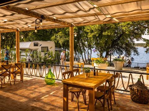 Terraza de restaurante con mesas de madera y vistas al mar y autocaravanas en Valamar Camping Istra, Istria.