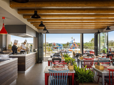 Restaurant moderne avec cuisine ouverte et vue sur l’aire de jeux aquatique au Valamar Camping Istra, Istrie.