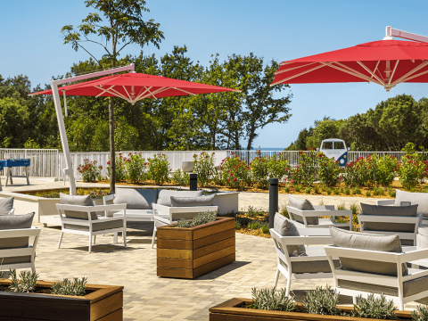 Area lounge esterna con sedie bianche, ombrelloni rossi e vegetazione al Valamar Camping Istra, Croazia.