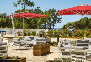 Area lounge esterna con sedie bianche, ombrelloni rossi e vegetazione al Valamar Camping Istra, Croazia.