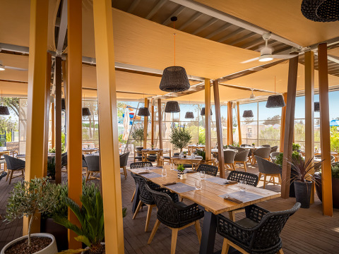 Terrasse de restaurant moderne avec tables en bois et chaises en osier au Valamar Camping Istra, en Croatie.