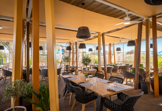 Moderne restaurantterrasse med træborde og flettede stole, omgivet af grønne planter på Valamar Camping Istra.