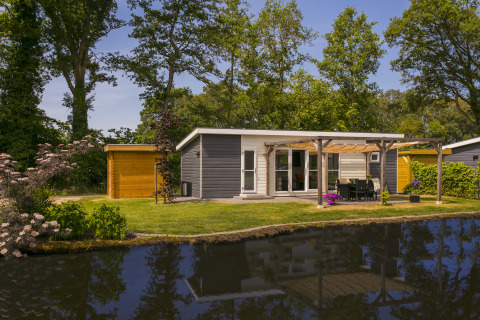Chalet de vacances à De Lochemse Berg, Pays-Bas, avec terrasse au bord de l’eau et jardin arboré ensoleillé.