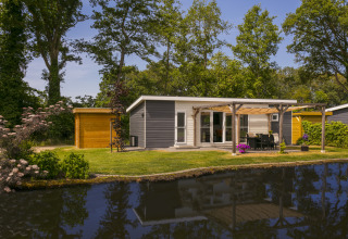 Chalet de vacances à De Lochemse Berg, Pays-Bas, avec terrasse au bord de l’eau et jardin arboré ensoleillé.