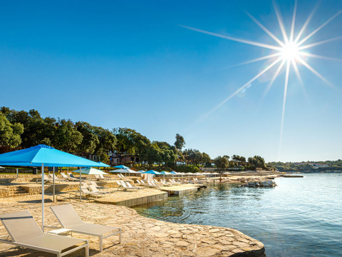 Zonnige oever bij Valamar Camping Istra in Istrië, Kroatië, met ligzetels, parasols en rustig water.