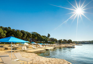 Soleada zona costera de Valamar Camping Istra en Istria, Croacia, con tumbonas, sombrillas y aguas tranquilas.