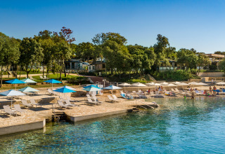 Strandbeeld bij Valamar Camping Istra in Kroatië met ligbedden, parasols en helderblauw water.