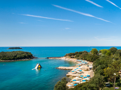 Vue panoramique de Valamar Camping Istra en Istrie, Croatie, avec plage, parasols bleus et mer cristalline.